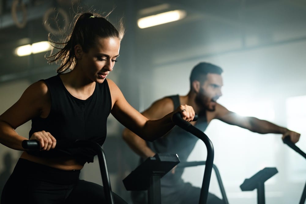 Kobieta i mężczyzna ćwiczący na rowerach stacjonarnych — cardio vs trening siłowy